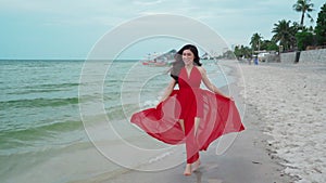 Slow-motion of cheerful woman in red dress walking on sea beach