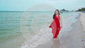 Slow-motion of cheerful woman in red dress walking on sea beach