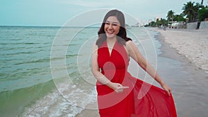 Slow-motion of cheerful woman in red dress walking on sea beach