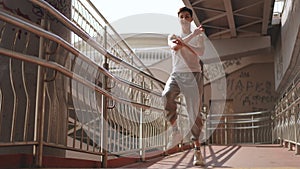 Slow motion. Cheerful young guy energetically moves his body and arms while standing under a city bridge outdoors. The