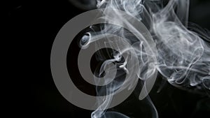 SLOW MOTION: Cigarette smoke lifts up on a dark background