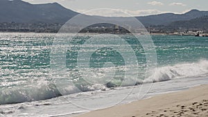 Slow motion Clear blue waves with strong wind on a sandy empty beach in Cannes with Theoule-sur-Mer on background