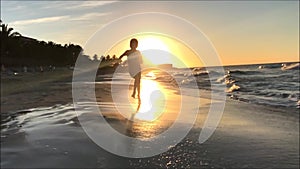 Slow motion clip of a young boy running on a beach towards camera against a sunset