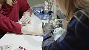 A slow motion close up filming of a young blonde beautician in a shirt cleaning with a sponge the nails of a client on