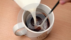 SLOW MOTION CLOSE UP looking into a mug as milk is added to cocoa powder and stirred with a teaspoon