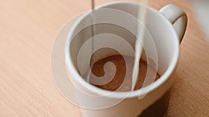 SLOW MOTION CLOSE UP looking into a mug as a teaspoon stirs milk as it`s added to cocoa powder