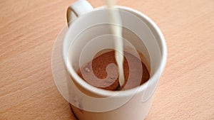 SLOW MOTION CLOSE UP of milk being poured into a mug of cocoa powder