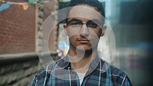 Slow motion close-up portrait of good-looking young Arab man wearing glasses looking at camera with serious face