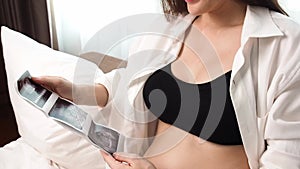 Slow motion. Close up pregnant belly Pregnancy mother looking at ultrasound film and touching her abdomen. Asian pregnancy woman s