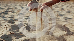 SLOW MOTION, CLOSE UP: The sand passes through the fingers of a young woman. The sand is running through fingers of a