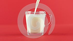 Slow motion close-up shot of cold diary milk cold beverage drink pooring into glass cup with facets red background in