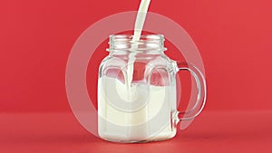 Slow motion close-up shot of cold diary milk cold beverage drink pooring into glass jar mug red background in studio