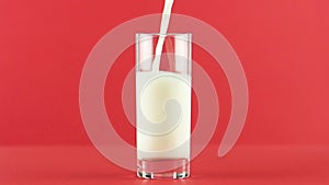 Slow motion close-up shot of cold diary milk cold beverage drink pooring into glass red background in studio