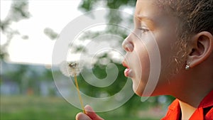 Slow Motion Close-Up Shot of Cute Little Girl Carefree Blowing a Dandelion Outdoors on a Sunset. Concept of Happy