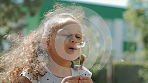 Slow Motion Close-Up Shot of Cute Little Girl Carefree Blowing a Dandelion Outdoors on a Sunset. Concept of Happy