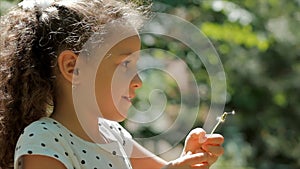 Slow Motion Close-Up Shot of Cute Little Girl Carefree Blowing a Dandelion Outdoors on a Sunset. Concept of Happy