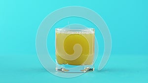 Slow motion close-up shot of fruit orange multifruit juice cold beverage drink pooring into low glass with facets blue
