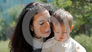 Slow Motion Close-Up Shot of Happy Mother Hugging Her Child and Gently a Carefree Blowing a Dandelion Outdoors. Concept