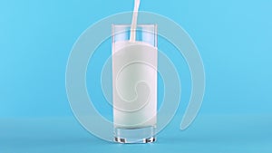 Slow motion close-up shot of milk cold beverage drink pooring into glass blue background in studio