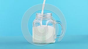 Slow motion close-up shot of milk cold beverage drink pooring into glass jar blue background in studio
