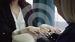 Slow motion close up showcase with camera floating of a blonde beautician in black gloves cleaning client`s nails with