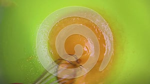 Slow motion close-up of someone preparing a homemade omelet or for baking mix eggs with a metal whisk in a plastic bowl. The proce