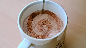 SLOW MOTION CLOSE UP of a teaspoon mixing milk and cocoa powder in a mug