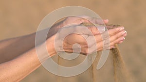 Slow motion close up, unrecognizable woman hands grabs a handful of dry sand and lets it fall between her fingers. Young