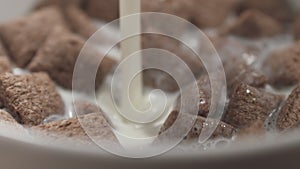 Slow motion closeup pouring milk into bowl with cereal chocolate pillows for breakfast