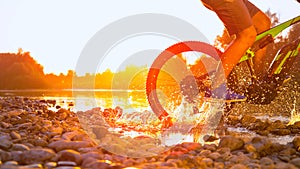 SLOW MOTION CLOSEUP Unrecognizable man MTB biking in shallow river at sunset