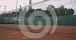 Slow Motion commercial footage of tennis practice through the tennis court net. Straight view of a female athlete