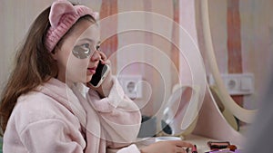 Slow motion. Cute fashionista talking on a mobile phone with patches under eyes. A girl, in a bathrobe and a pink