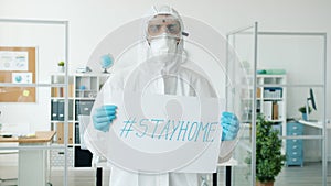 Slow motion of doctor in protective suit standing in empty office with stayhome poster