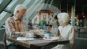 Slow motion of elderly man giving gift box to excited woman during lunch in cafe