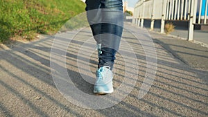 Slow motion female legs in blue jeans and sneakers walking on asphalt path way in sunny city. Woman in jeans and sport