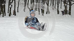 Slow motion footage of a boy gleefully gliding down a snow-covered hill on his plastic sled, grinning from ear to ear.