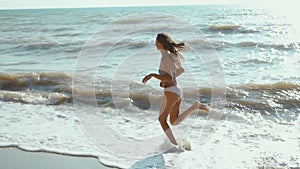 slow motion footage of happy joyful fitness girl in bikini running along sea beach with waves