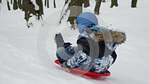 Slow motion footage of a happy and smiling young boy gleefully sliding down a snowy hill on his plastic sled.