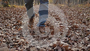 Slow motion footage of men's feet walking on fallen leaves, lifting them up. Men's feet in brown sneakers and blue jeans