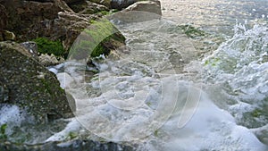 Slow motion footage of sea waves rolling on beach and breaking over rocks and cliffs with growing seaweeds and algae.