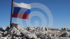 Slow-motion footage of the tattered Russian flag developing in the wind. The flag is set on top of the mountain. In the background