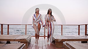 Slow motion footage of two attractive girls walking sensually in summer stylish clothes in same colors. Seaside area