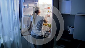Slow motion footage of young woman takes apple from refrigerator. Girl eaitng at night