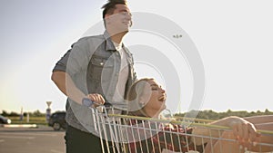 Slow motion: a Free and cheerful man and woman ride in carts in a supermarket Parking lot, shouting and raising their