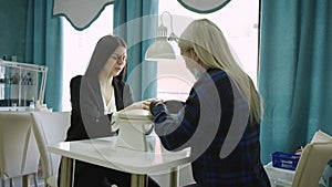 A slow motion general shot of a blonde beautician making a manicure for a client and listening to her speech