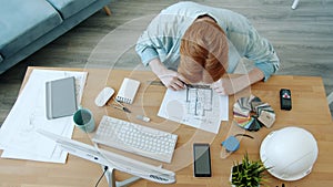 Slow motion of ginger-haired man architect working with building plan indoors at home