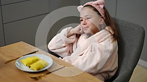 Slow motion. A girl in a bathrobe and a hair band on her head sits on a chair, with her head resting on her hand