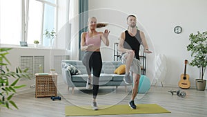 Slow motion of girl and guy in sportswear jumping doing sports indoors at home