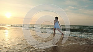 SLOW MOTION: Girl running in shallow water at sunset. A girl in a white dress is running at the water`s edge near the