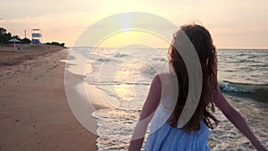 SLOW MOTION: Girl running in shallow water at sunset. A girl in a white dress is running at the water`s edge near the